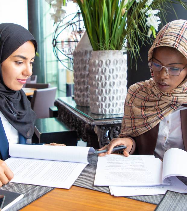 Confident female professionals checking documents. Young Muslim business women sitting in cafe and reading papers. Contract expertise concept